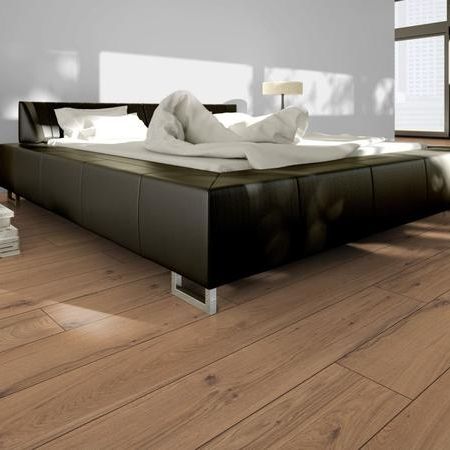 Schlafzimmer mit schwarzem Lederbett, warmem Holzfußboden, einer Stehlampe und einem leuchtend orangefarbenen Stuhl