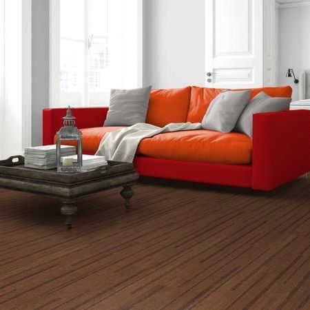 Eine leuchtend orangefarbene Couch mit einem grauen Kissen auf einem Holzboden neben einem dunklen Couchtisch