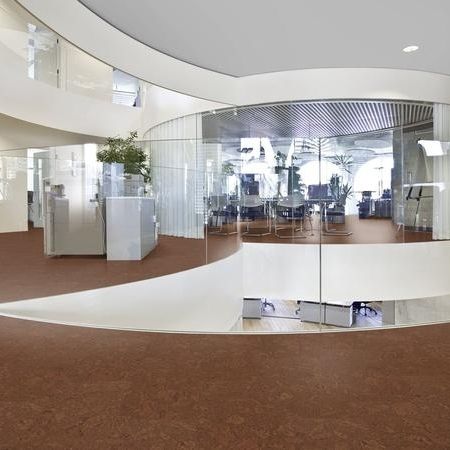 Eine moderne Bürolobby mit geschwungenen Glaswänden, braunem Bodenbelag und kreisförmigem Design
