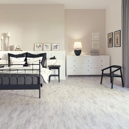 Stilvolles Schlafzimmer mit einem schwarzen Metallbett, grauer Bettwäsche, Nachttischlampen, weißer Kommode und Kunstwerken