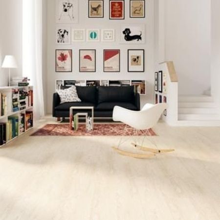 Helles Wohnzimmer mit schwarzer Couch, farbenfroher Kunst an der Wand, einem Schaukelstuhl und einem gemütlichen Teppich auf hellem Holzfußboden