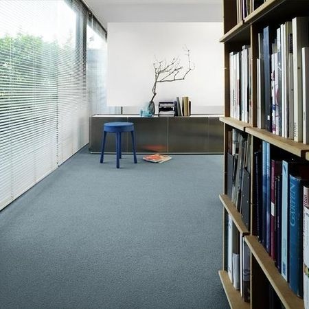 Modernes Interieur mit einem blauen Teppich, einem minimalistischen Bücherregal und einem kleinen blauen Hocker