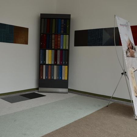 Eine Ecke einer modernen Einrichtung mit einem bunt bestückten Bücherregal, Stoffmustern an den Wänden und einem Werbebanner